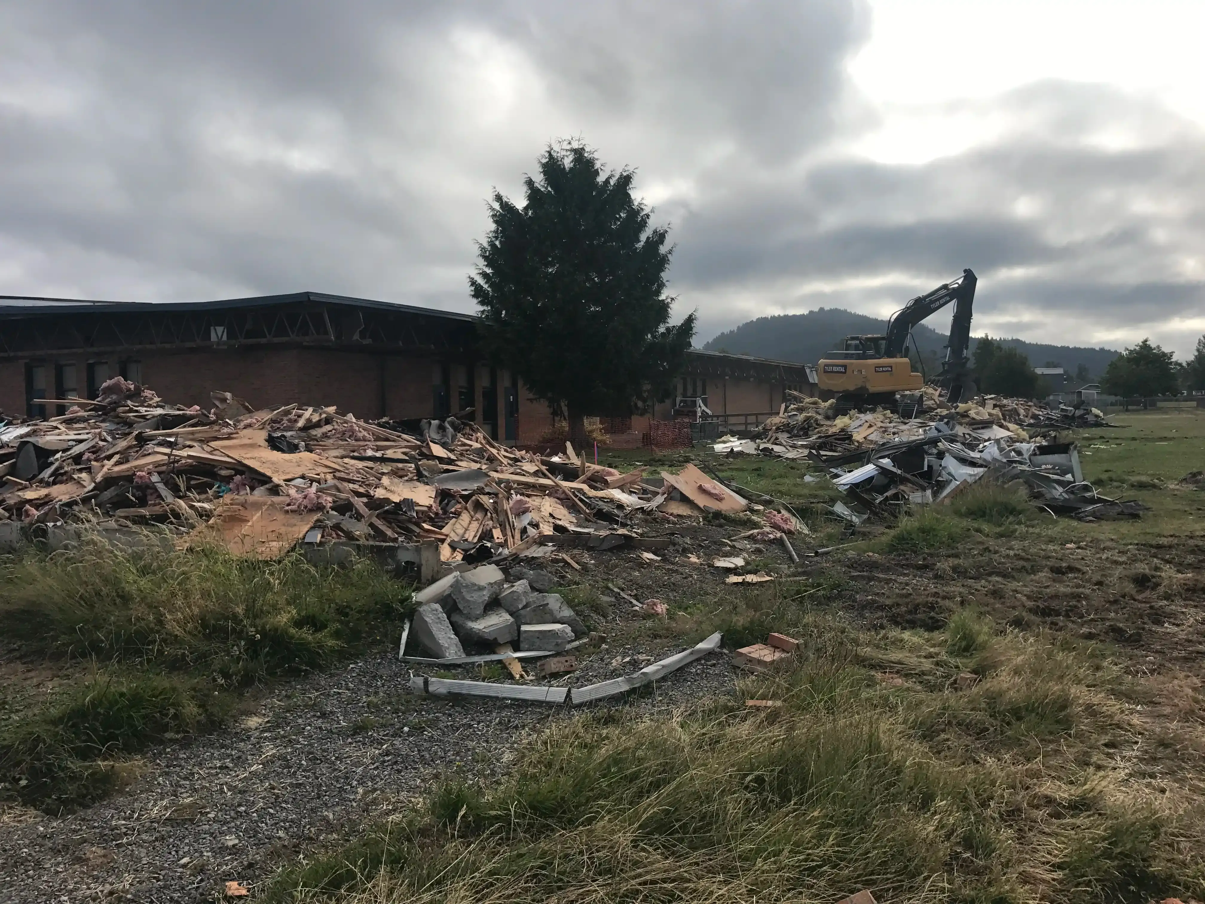 Photo of piles of demolition rubble with an excavator on top of one of the mounds. Photo of piles of demolition rubble with an excavator on top of one of the mounds.