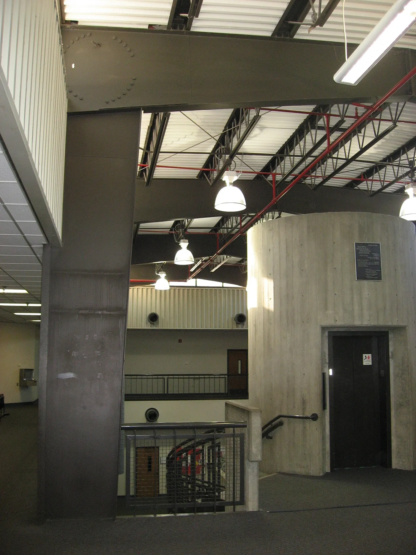 Photo of old interior second-level of the building showing exposed concrete elevator shaft and drab gray colors.