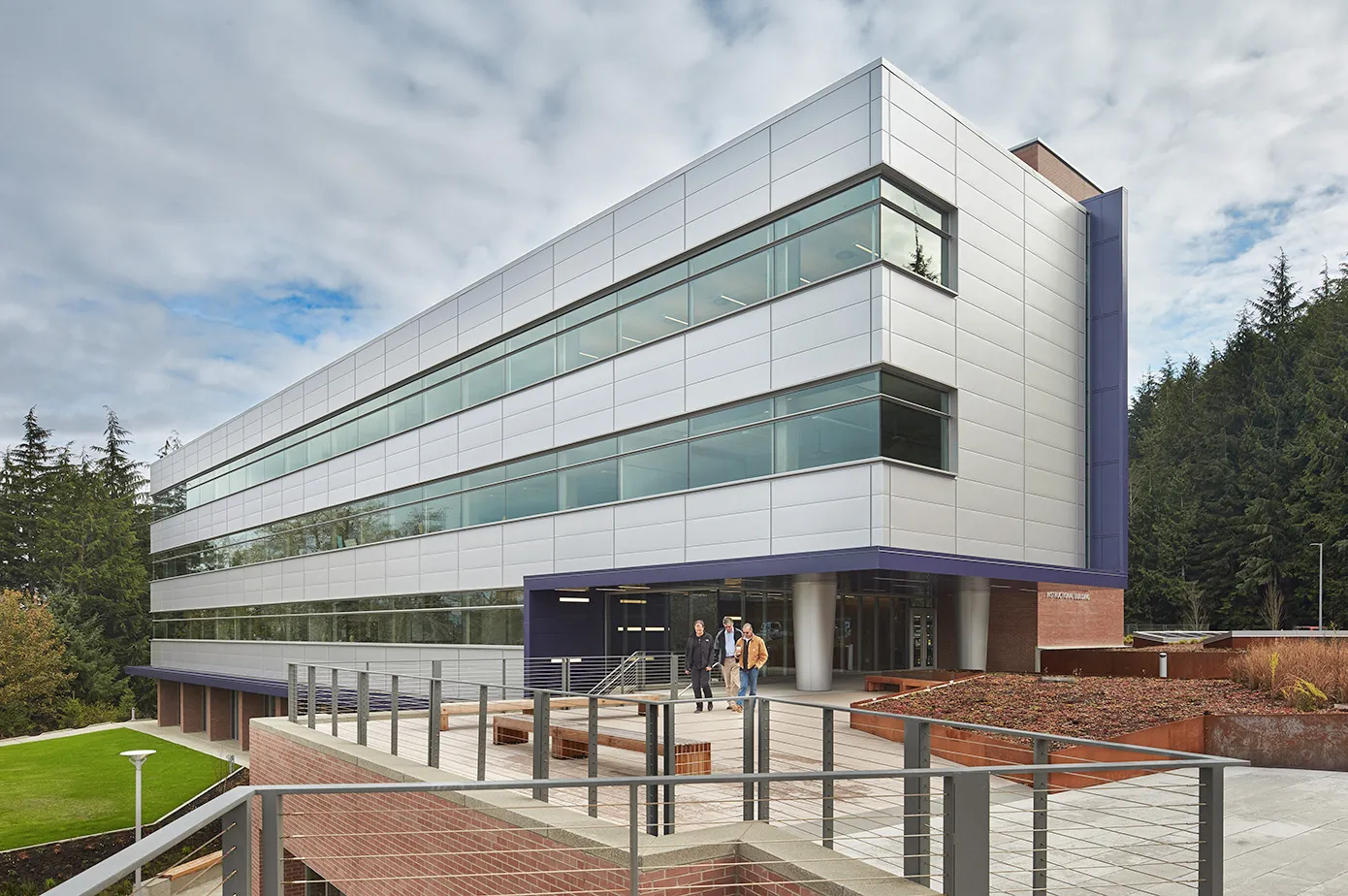 Photo taken from the Northeast direction of the exterior of the new building showcasing the metal-clad siding and end-to-end storefront windows.