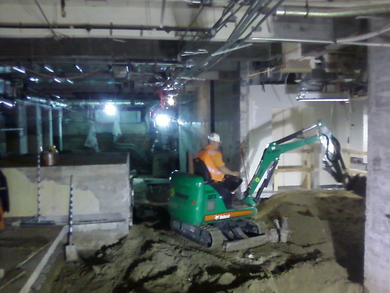 Photo of a worker operating a small excavator inside a building, removing material from below the floor.