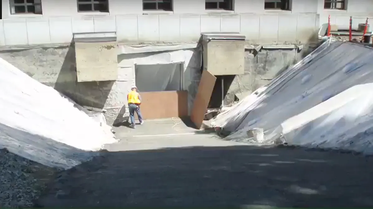 Photo, taken from outside, of the temporary concrete ramp at the west end of the building down to the basement floor level.