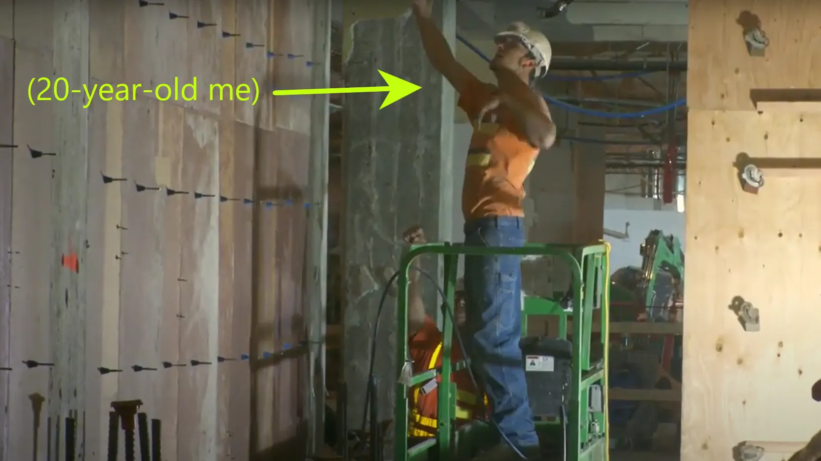 20-year-old Ryan in a scissor lift talking to a co-worker and pointing above his head.