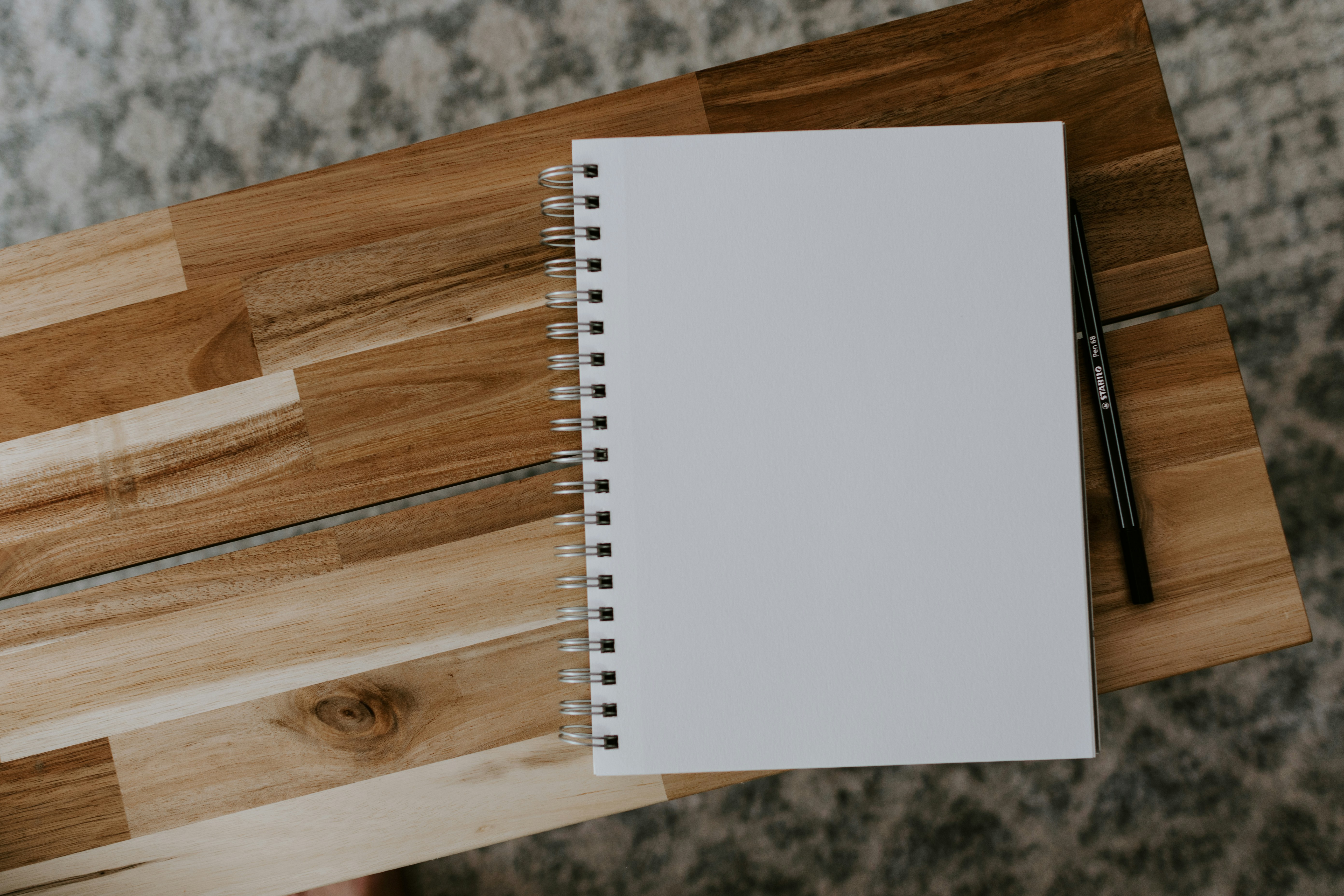 A Notebook turned to a blank sheet with a pen on a small empty wood-grain endtable.